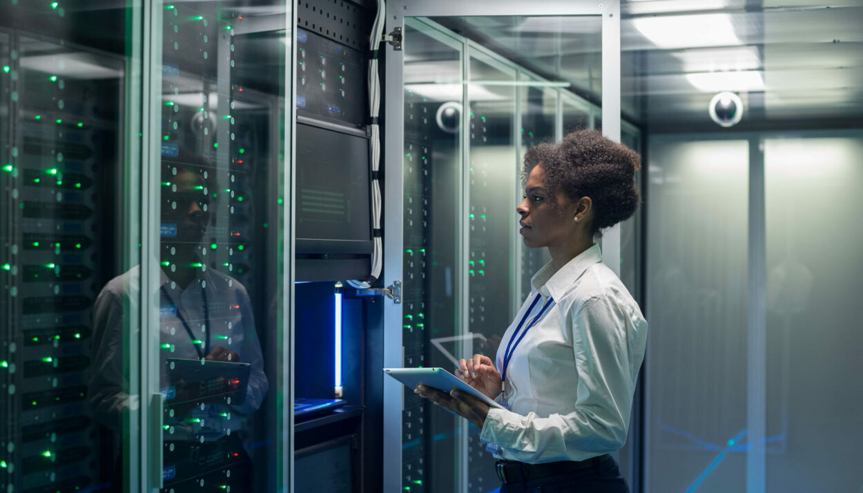 Medium shot of female technician working on a tablet in a data center full of rack servers running diagnostics and maintenance on the system