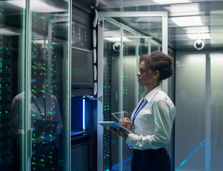 Medium shot of female technician working on a tablet in a data center full of rack servers running diagnostics and maintenance on the system